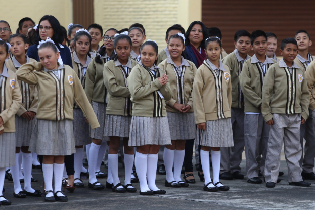 Eine Gruppe von Kindern in Schuluniformen, die vor einem Gebäude mit einer Wand und einem Rollladen im Hintergrund stehen.