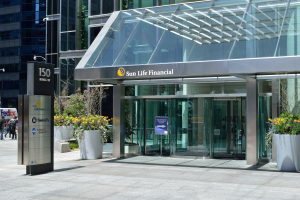 Moderner Glaswand-Sun Life Financial-Gebäude in Toronto mit einem Schild, Topfpflanzen mit Blumen, Passanten, einem Straßenpfosten, einem Schild, Fahrzeugen auf der Straße und einem bewölkten Himmel.