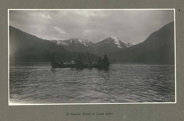 Schwarzes und weißes Foto einer Familie in einem Kanu auf einem See mit Bergen und Bäumen im Hintergrund, Himmel oben sichtbar, Text unten.