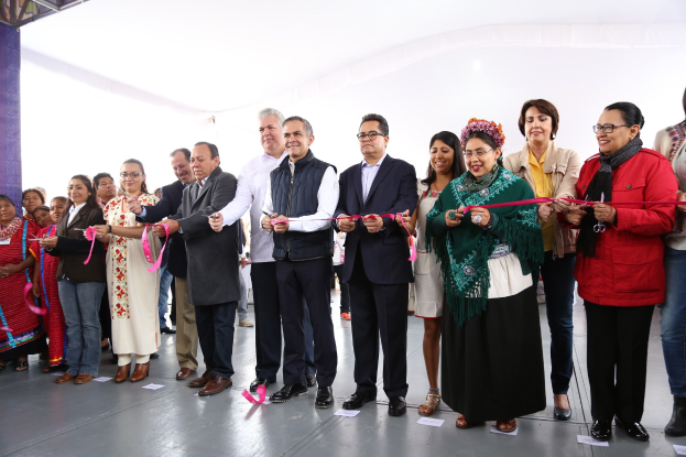 Eine Gruppe von Menschen bei einer Scherenschnitte-Zeremonie, die eine Schere halten, mit einer Säule links daneben, verstreuten Papieren auf dem Boden und einem weißen Tuch im Hintergrund.