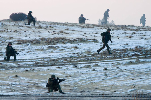 Eine Gruppe von Soldaten in Helmen und mit Gewehren in der Hand überquert ein schneebedecktes Feld mit Pflanzen im Hintergrund und einem klaren Himmel darüber, mit Text am unteren Bildrand.