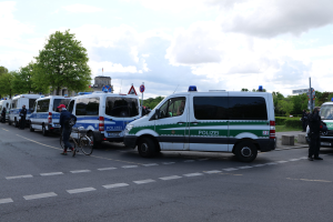 Eine Gruppe von Polizeiwagen, die entlang einer Straße geparkt sind, mit einem Radfahrer im Vordergrund und Gebäuden, Bäumen, Schildern und anderen Elementen im Hintergrund.