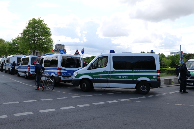 Eine Gruppe von Polizeiwagen, die entlang einer Straße geparkt sind, mit einem Radfahrer im Vordergrund und Gebäuden, Bäumen, Schildern und anderen Elementen im Hintergrund.