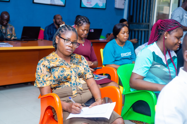 Eine Gruppe von Menschen sitzt in einem Raum mit Laptops, Büchern und anderen Gegenständen auf Tischen während einer scheinbaren Schulung über Bildung in Ghana.